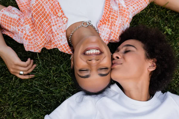 Vista dall'alto di felice donna africana americana lesbica baciare fidanzata e sdraiata sull'erba — Foto stock
