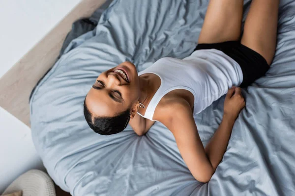 Вид зверху усміхненої афроамериканської жінки з закритими очима, спираючись на ліжко — стокове фото