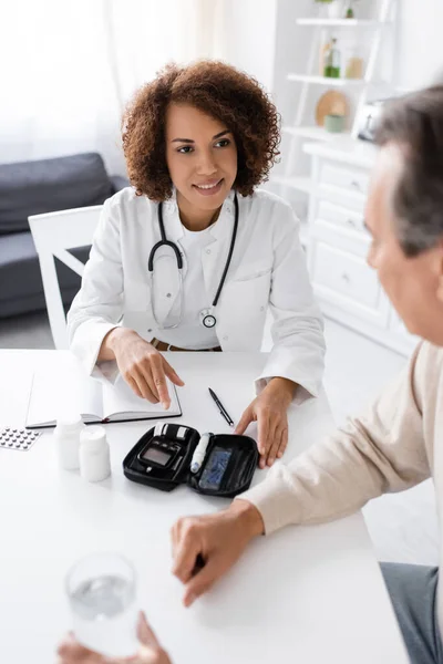 Smiling african american doctor looking at middle aged man with diabetes — Stock Photo