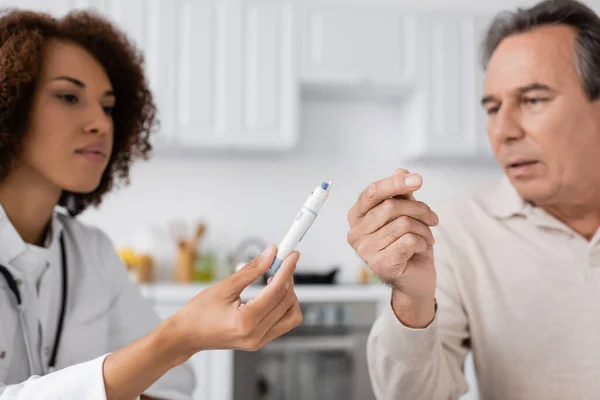 Curly african american doctor showing lancet pen to middle aged patient — Stock Photo