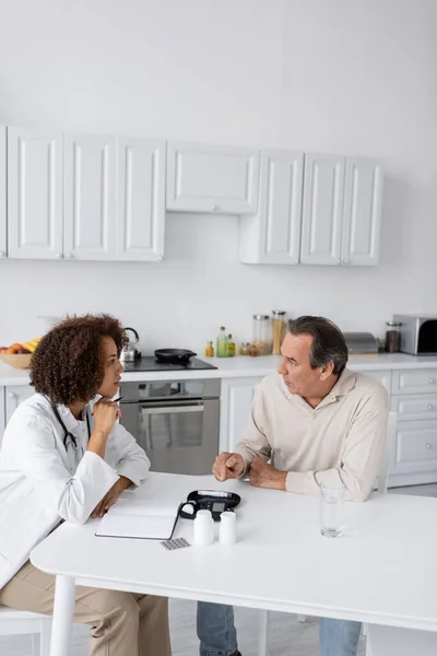 Middle aged man with diabetes talking with curly african american doctor in white coat — Stock Photo