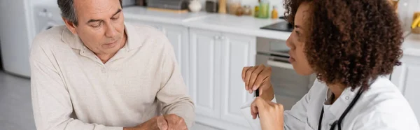 Чоловік середнього віку з діабетом розмовляє з кучерявим афроамериканським лікарем у білому пальто, банер — стокове фото
