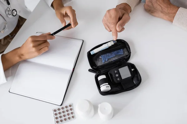 Vue de dessus de l'homme d'âge moyen avec le diabète pointant vers lancet stylo dispositif près médecin afro-américain — Photo de stock