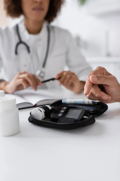 Обрезанный вид мужчины средних лет с диабетом, указывающим на устройство глюкометра рядом с африканским врачом-американцем — стоковое фото