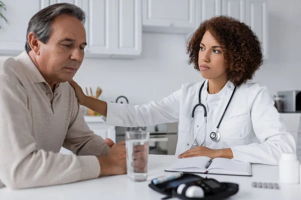 Young african american doctor in white coat calming upset middle aged man with diabetes — Stock Photo