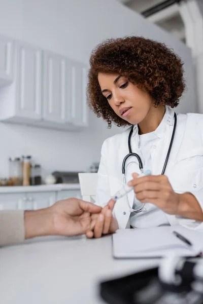 Curly african american doctor taking blood sample of middle aged man with lancet pen — Stock Photo