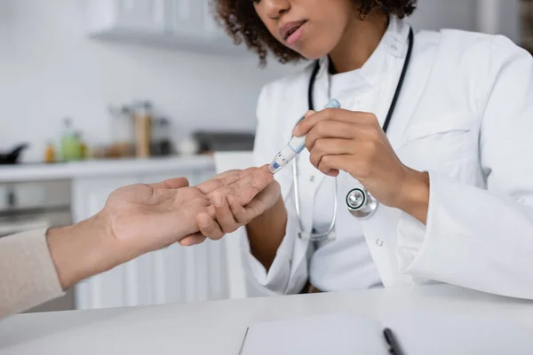Cropped view of curly african american doctor taking blood sample of middle aged man with lancet pen — Stock Photo