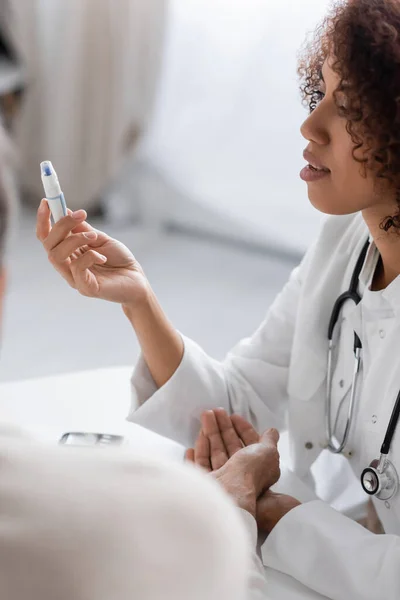 Young and curly african american doctor holding lancet pen device near blurred patient — Stock Photo