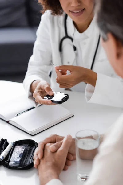 Visão recortada do médico afro-americano em casaco branco segurando dispositivo de glicosímetro e tira de teste perto de paciente de meia-idade — Fotografia de Stock