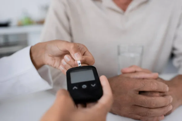 Teilansicht eines afrikanisch-amerikanischen Arztes, der einem Patienten mittleren Alters Teststreifen am Glukometergerät zeigt — Stockfoto