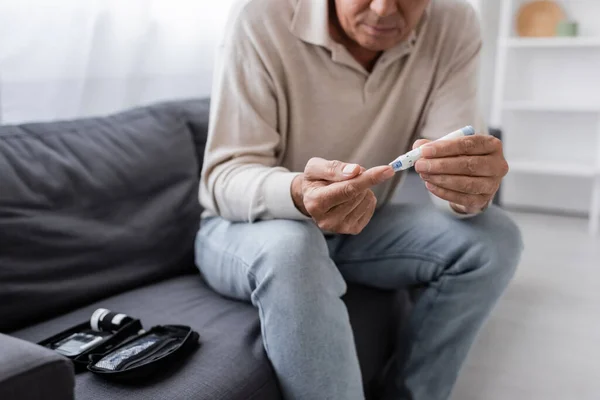 Ausgeschnittene Ansicht eines Mannes mittleren Alters mit Diabetes, der Blutprobe nimmt, während er auf der Couch im Wohnzimmer sitzt — Stock Photo