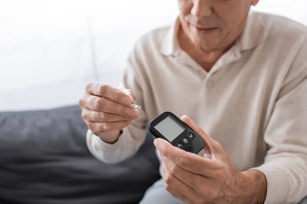 Vista recortada del hombre de mediana edad con diabetes que sostiene el dispositivo medidor de glucosa y la tira de prueba - foto de stock