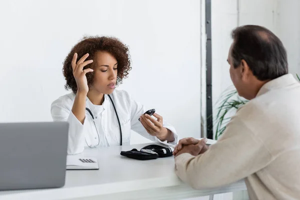 African american doctor looking at glucometer and talking with middle aged patient with diabetes — Stock Photo