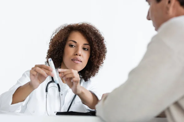 Jeune médecin afro-américain pointant du doigt un stylo lancette près d'un patient d'âge moyen flou atteint de diabète en clinique — Photo de stock