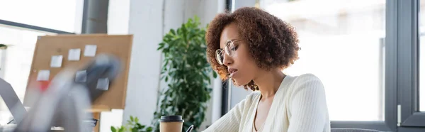 Donna d'affari afroamericana seduta vicino a laptop sfocato e caffè per andare in ufficio, striscione — Foto stock