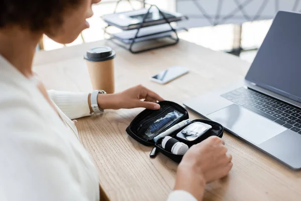 Vista recortada de la mujer de negocios afroamericana sosteniendo kit de diabetes cerca de gadgets y café en la oficina - foto de stock