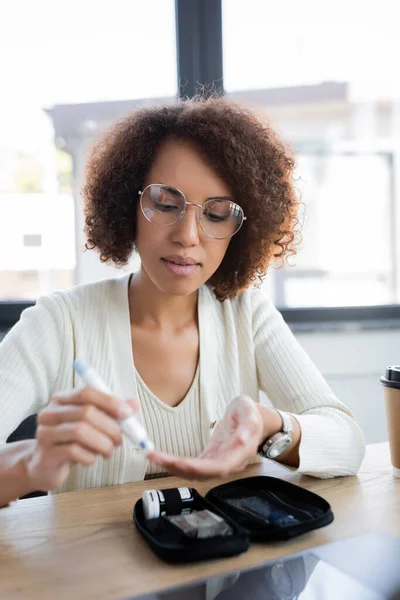 Африканская американская бизнесвумен, использующая размытое перо Ланцета рядом с набором для лечения диабета в офисе — стоковое фото