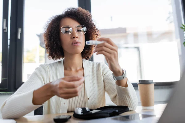 African american businesswoman looking at glucometer lancet near laptop in office — Stock Photo