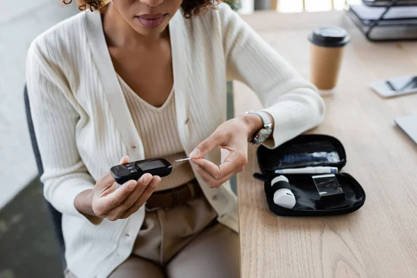 Cropped view of african american businesswoman holding glucometer in office — Stock Photo
