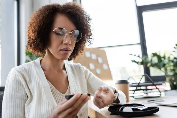 Femme d'affaires afro-américaine dans les lunettes de contrôle de la glycémie avec glucomètre au bureau — Photo de stock