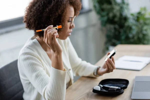 Donna d'affari afroamericana offuscata con siringa per il diabete e glucometro in ufficio — Foto stock