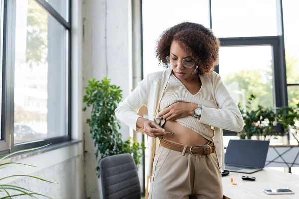 African american businesswoman in eyeglasses doing insulin injection in belly in office — Stock Photo
