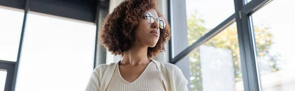 Visão de baixo ângulo da empresária afro-americana em óculos olhando para longe no escritório, banner — Fotografia de Stock