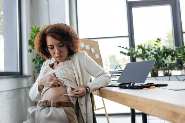 Empresária afro-americana com diabetes fazendo injeção de insulina perto de kit médico e laptop no escritório — Fotografia de Stock