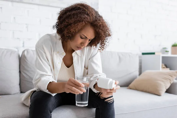 African american woman with diabetes feeling bad while holding pills and water on couch at home — Stock Photo