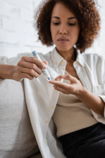 Blurred african american woman with diabetes using lancet pen in living room — Stock Photo