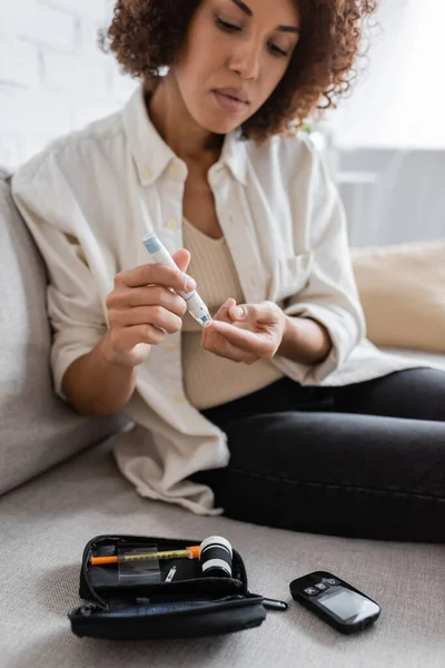 Jovem afro-americana com o uso de caneta lancet perto do kit de diabetes no sofá — Fotografia de Stock