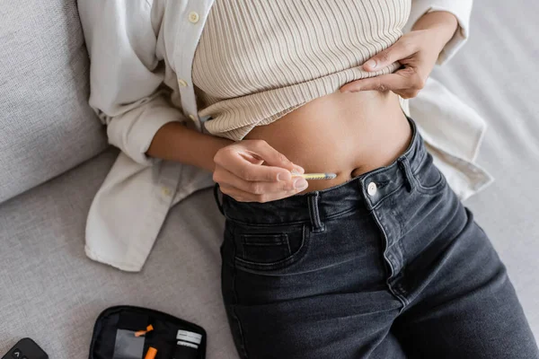 Вид сверху на африканскую женщину, делающую инсулин в животе рядом с диабетическим комплектом дома — стоковое фото