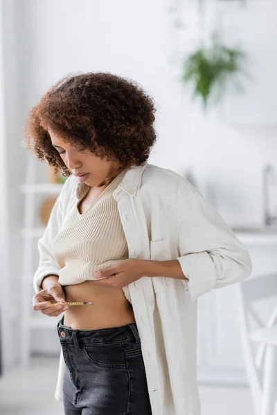 Young african american woman with diabetes holding syringe while doing insulin injection at home — Stock Photo