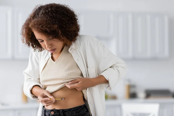 Curly african american woman with diabetes doing injection of insulin in belly at home — Stock Photo