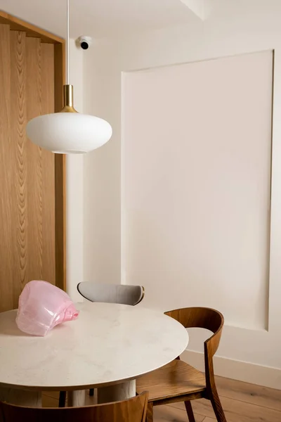 Decorative pink figurine on round dining table near wooden chairs in hotel room with security camera - foto de stock