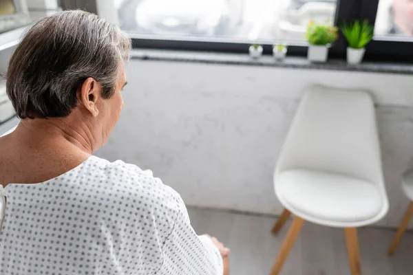 Elderly man in patient gown looking away in blurred hospital ward — Stock Photo