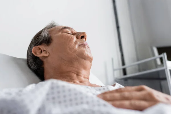 Low angle view of sick elderly man lying on bed in hospital ward — Stock Photo