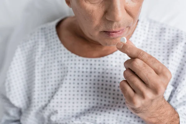 Cropped view of senior patient holding pill on bed in hospital ward — Stock Photo