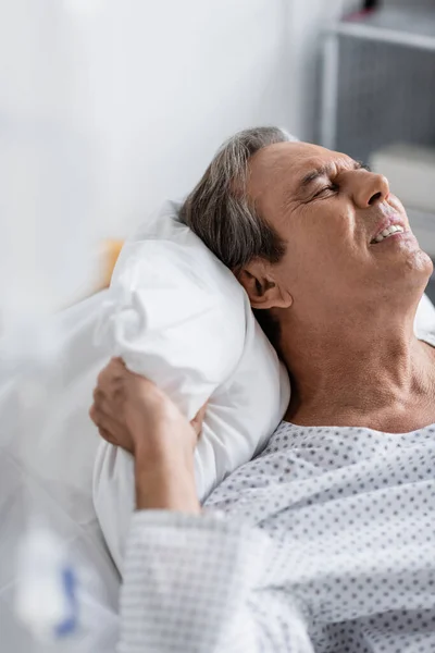 Paciente idoso doente que sofre de dor enquanto está deitado na cama na clínica — Fotografia de Stock