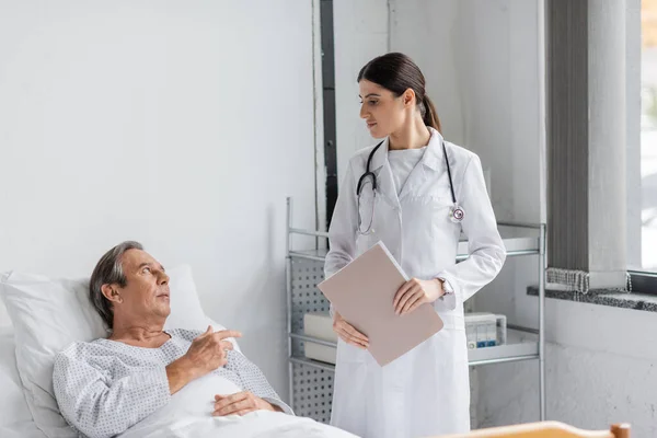Sick elderly patient talking to doctor with paper folder in hospital — Stock Photo