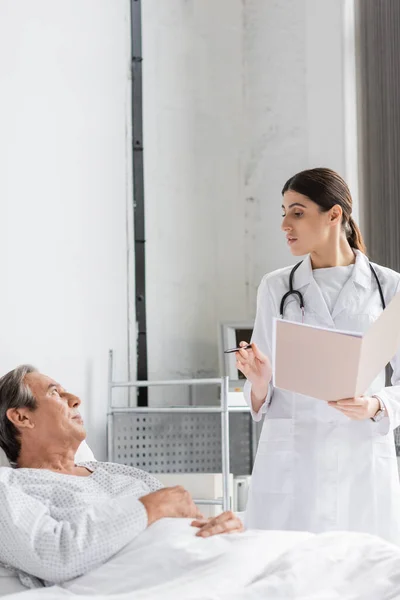 Doctor with paper folder talking to elderly patient in clinic — Stock Photo