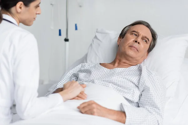 Blurred doctor touching hand of upset patient in hospital ward — Stock Photo
