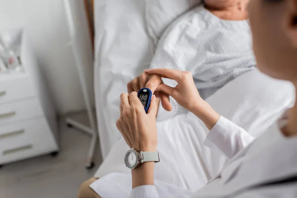 Vista ritagliata del medico che indossa il pulsossimetro al dito del paziente in clinica — Foto stock