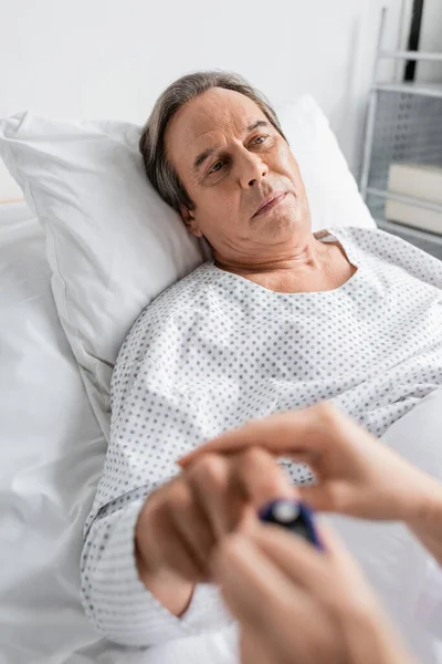 Blurred doctor wearing pulse oximeter on finger of patient in hospital ward — Stock Photo
