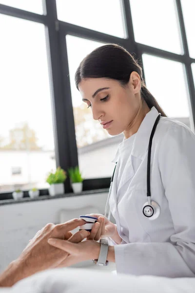 Brünette Ärztin trägt Pulsoximeter am Finger einer älteren Patientin auf Krankenhausstation — Stockfoto