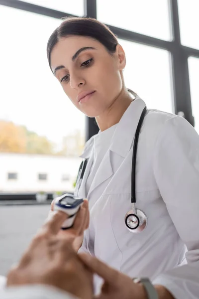 Doctor looking at pulse oximeter on finger of senior patient in hospital ward — Stock Photo