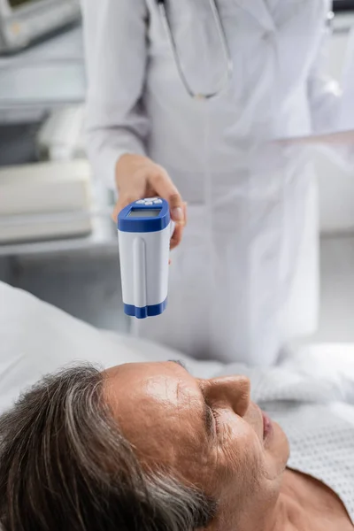 Verschwommener Arzt hält Pyrometer in der Nähe eines älteren Patienten auf Krankenhausstation — Stockfoto