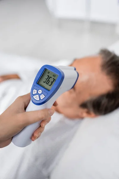 Doctor holding non-contact pyrometer near blurred patient in clinic — Stock Photo