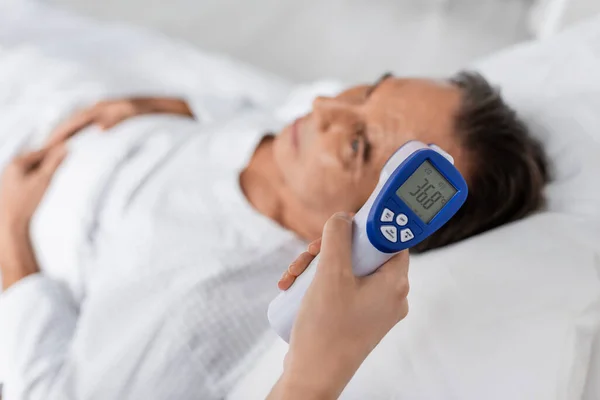 Arzt hält Pyrometer nahe verschwommenem älteren Patienten in Klinik — Stockfoto