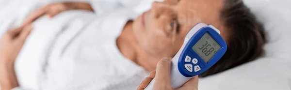 Doctor holding pyrometer near blurred patient on hospital bed, banner — Photo de stock